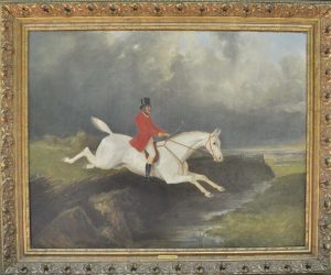 Gold framed oil painting of a man in foxhunting attire riding a white horse jumping over a river