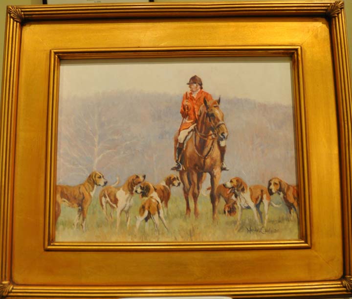Gold framed oil painting of a man in foxhunting attire on a horse in the field with foxhounds around him