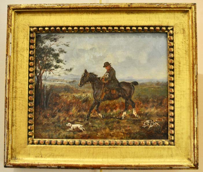 Gold framed oil painting of a man on a horse in a field with foxhounds