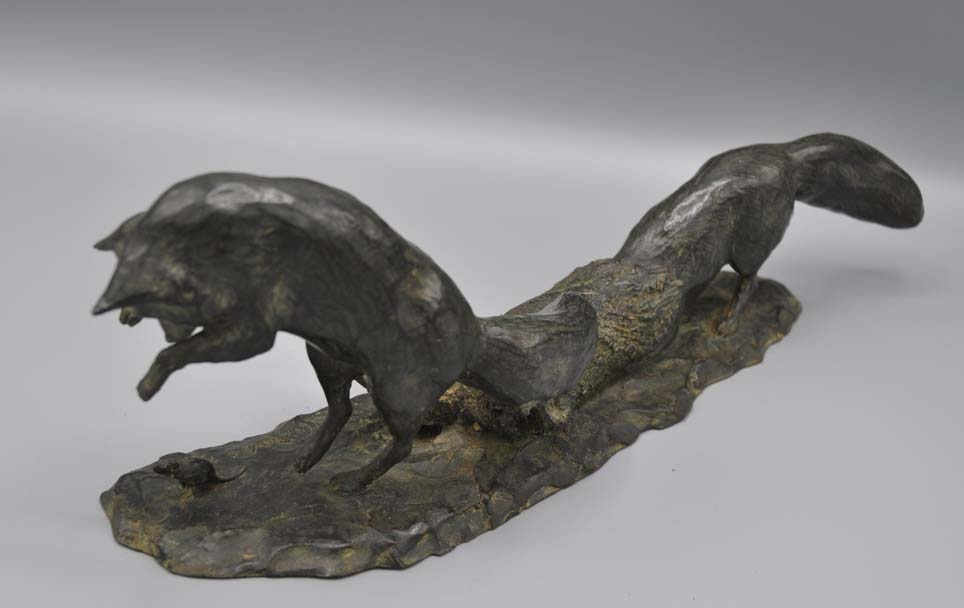 Bronze sculpture of a fox pouncing on a mouse and another fox crawling in a hollow log