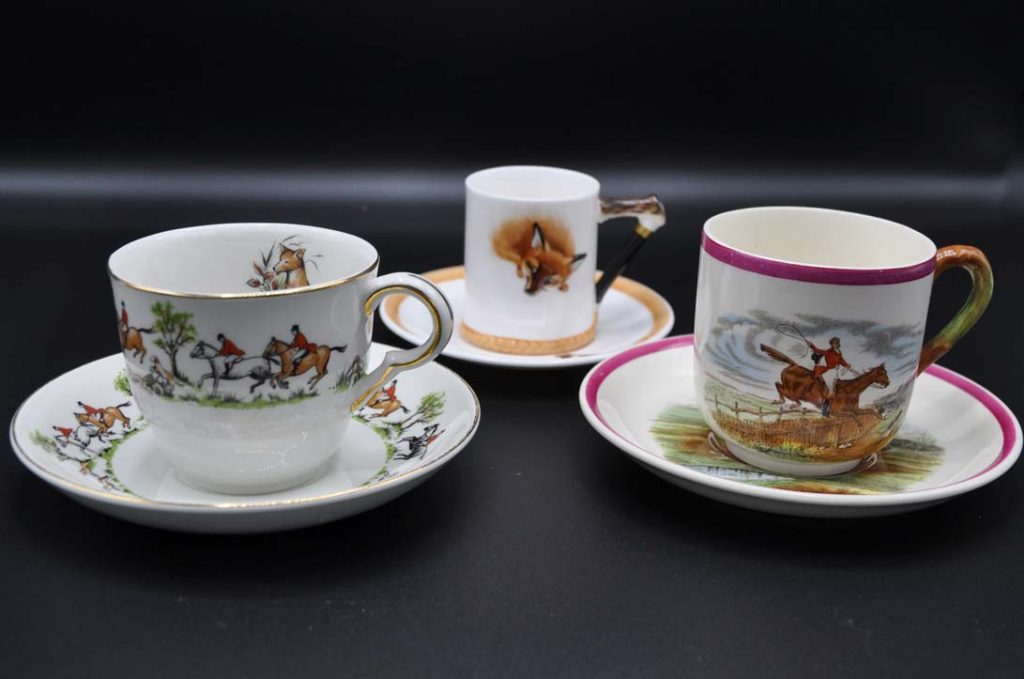 Painted china cup collection depicting a foxhunting scene with three riders and a pack of foxhounds