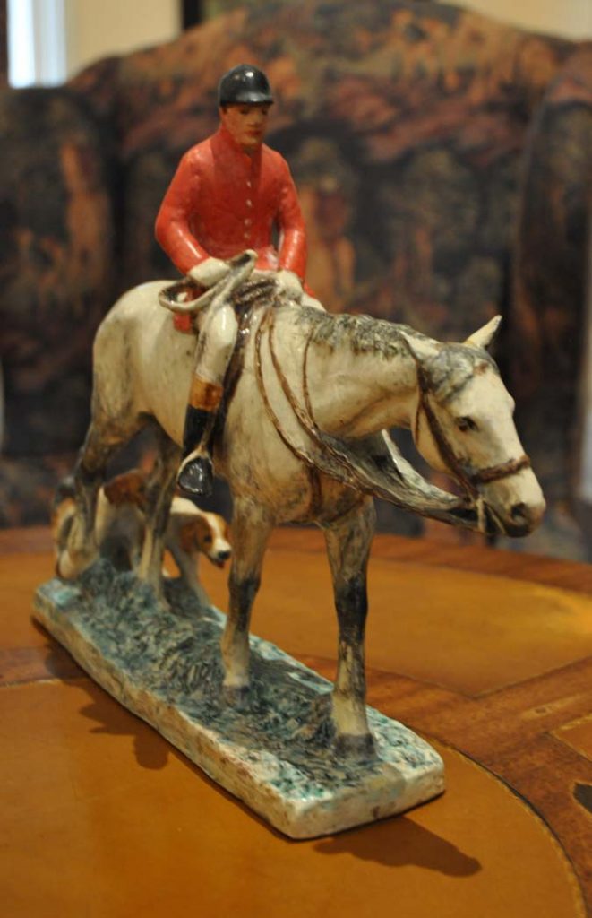 Figurine of a man in foxhunting attire riding a white horse with foxhounds following